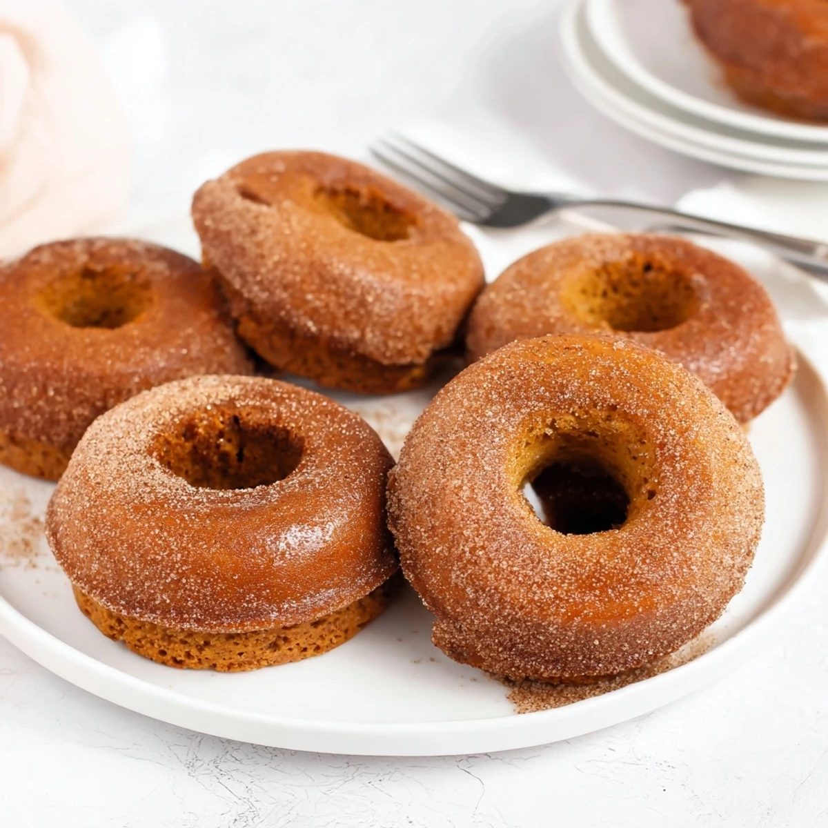 Moist vegan pumpkin muffin donuts dusted with cinnamon sugar for a cozy treat.