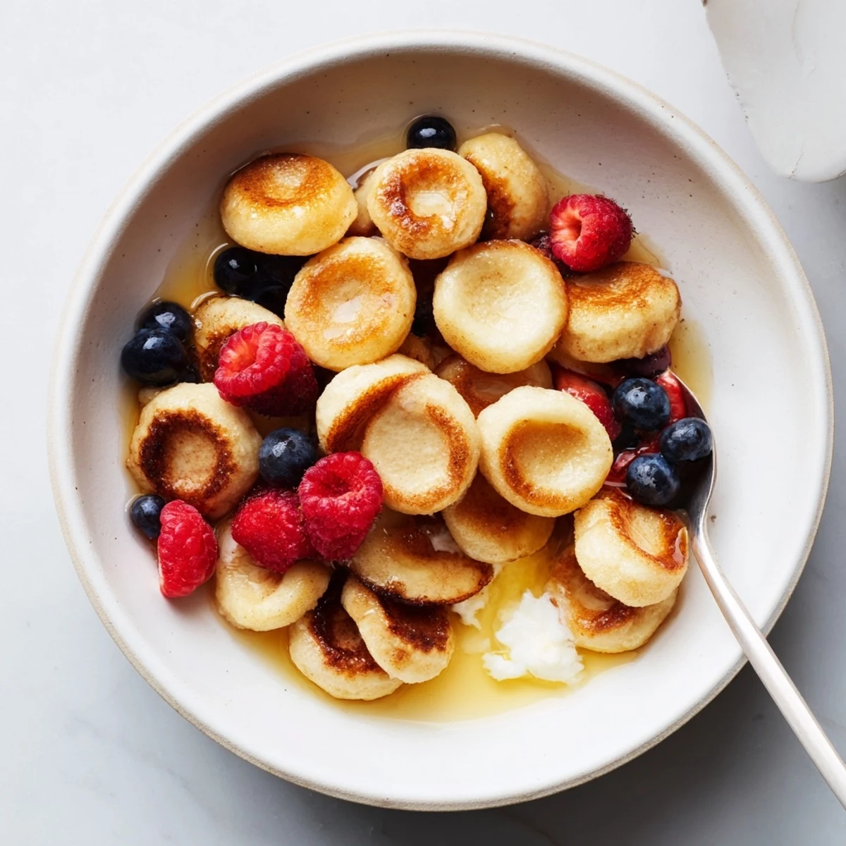 Delicious mini pancake cereal drizzled with maple syrup and fresh berries.