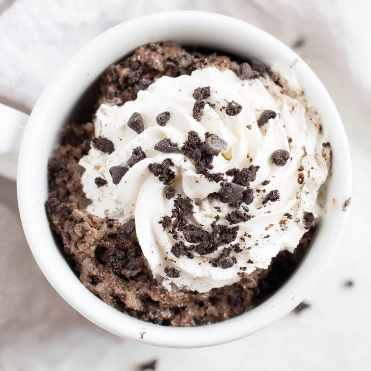 A warm, chocolatey Oreo mug cake, topped with a dollop of fresh whipped cream, ready to eat.