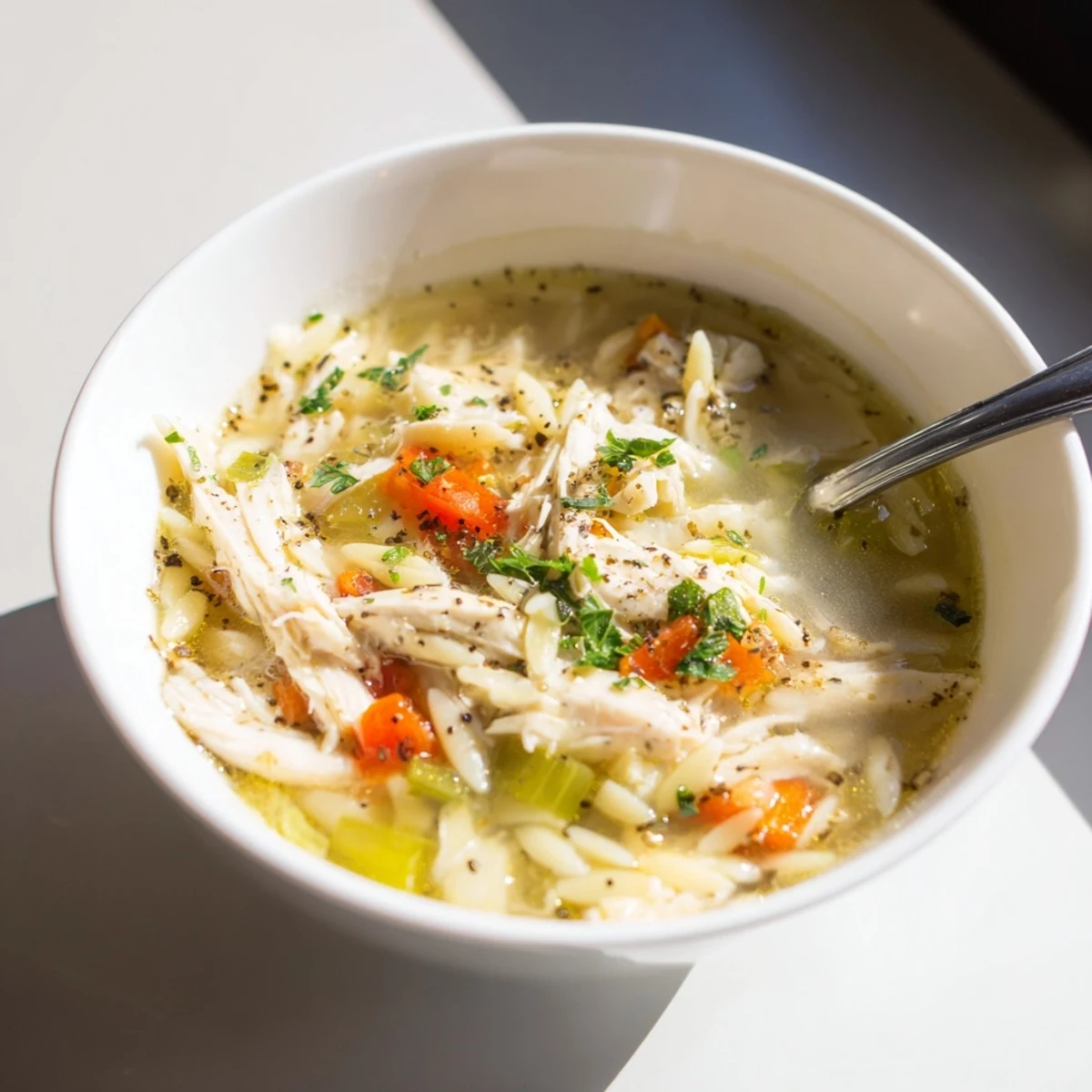 A warm bowl of Lemon Pepper Chicken Orzo Soup garnished with fresh parsley and lemon wedges.  