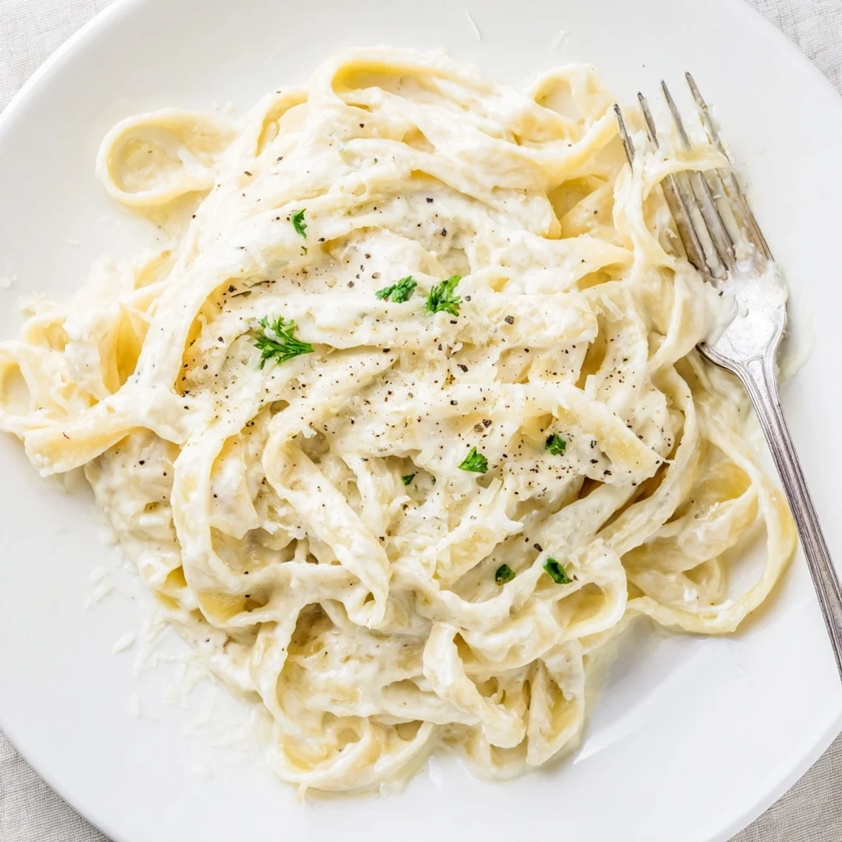 A close-up of Easy Creamy Cauliflower Alfredo over pasta, showing its creamy texture and garnished with chopped parsley.