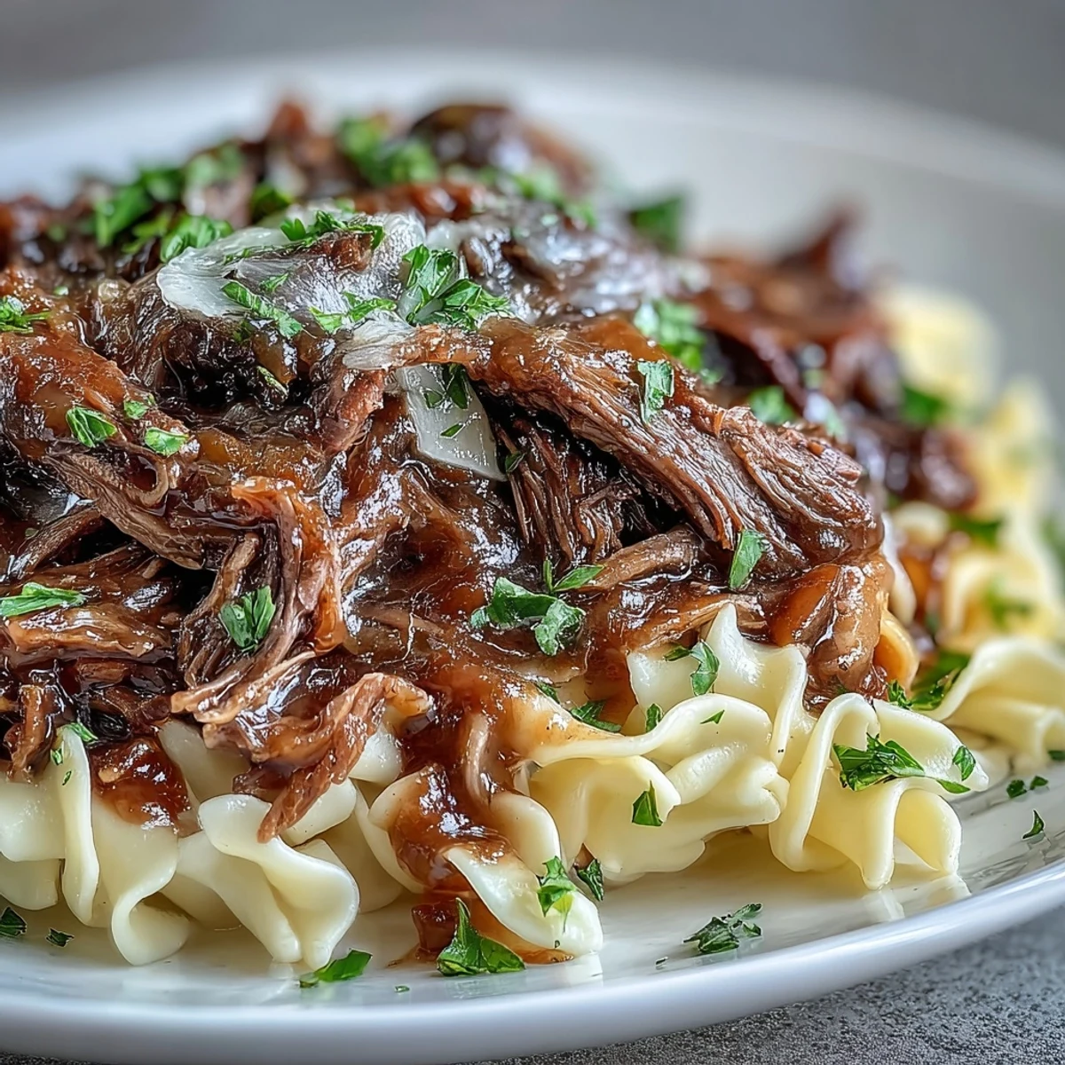A comforting bowl of Crockpot French Onion Pot Roast Pasta with juicy beef, melted Gruyère, and fresh parsley garnish on a rustic table.