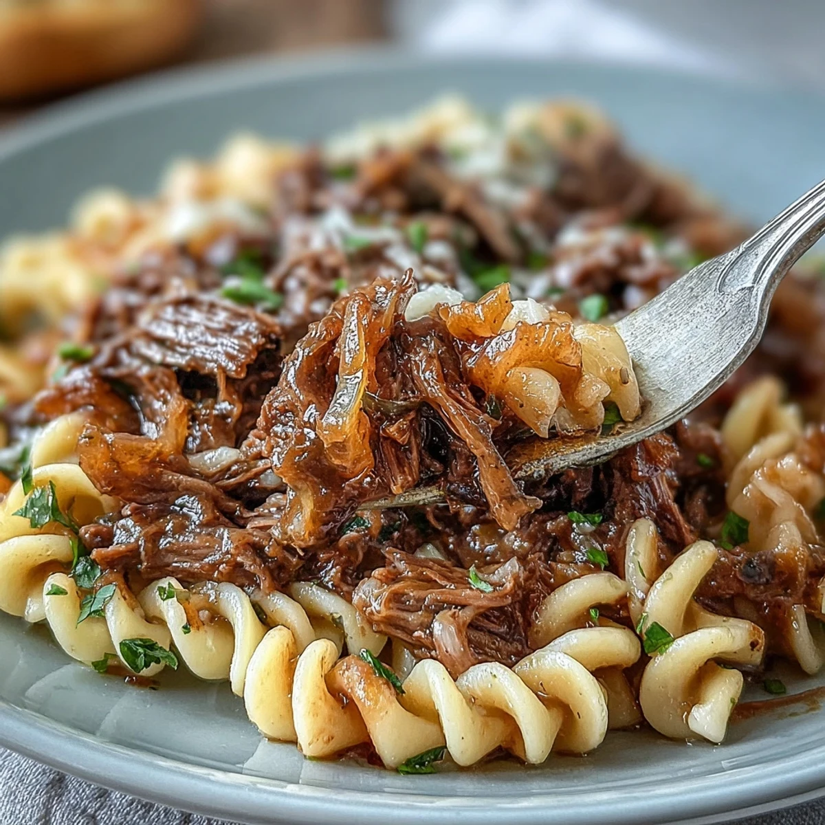 Hearty beef chuck roast simmered with wine and onions, shredded and served over wide egg noodles for a cozy meal.