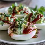 Vibrant avocado-filled deviled eggs topped with Sriracha sauce for a bold, tangy twist on a classic appetizer.