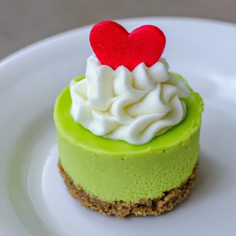 Bright green Grinch mini cheesecakes, topped with whipped cream and red heart sprinkles, ready to serve.