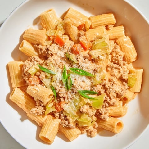 Steaming plate of Chaos Cooking Kimchi Ragu Pasta, topped with green scallions and Parmesan cheese, looks delicious.