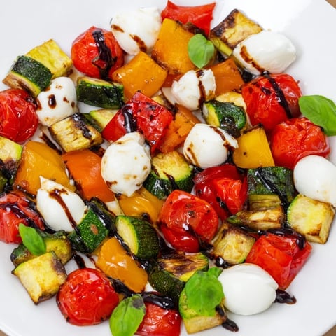 A vibrant platter of Roasted Veggie Caprese Salad showcases caramelized vegetables, creamy mozzarella pearls, and fresh basil with a balsamic drizzle.  