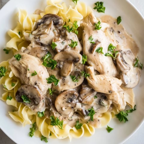 A close-up of creamy Chicken and Mushroom Stroganoff served over buttery egg noodles, garnished with fresh parsley.
