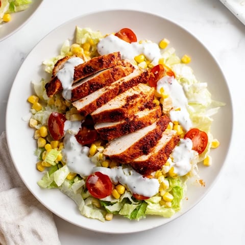 Sliced smoky BBQ chicken crowns a bed of crisp romaine lettuce, topped with grilled corn, black beans, cherry tomatoes, and creamy ranch drizzle.  