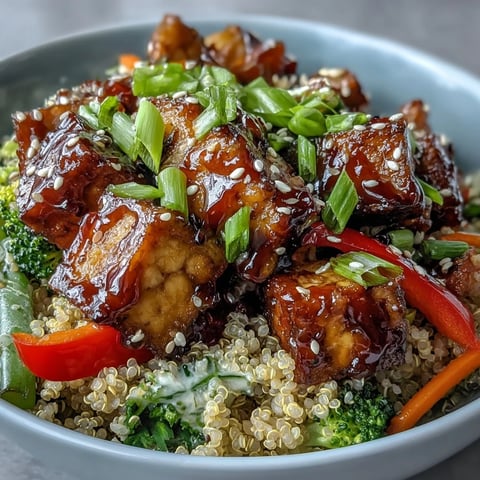 Golden crispy tofu cubes and vibrant stir-fried vegetables rest on fluffy quinoa, all generously drizzled with glossy homemade teriyaki sauce for a wholesome vegan dinner.