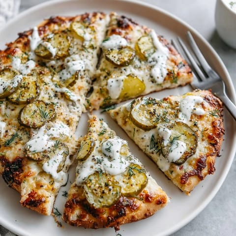 A close-up of a fresh pickle pizza, showing a creamy ranch drizzle over bubbling cheese.