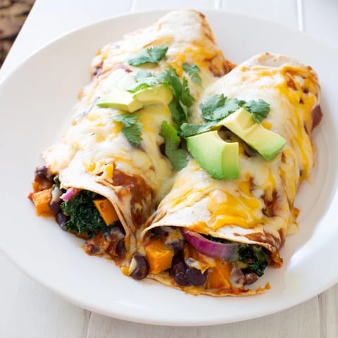 This one-pan sweet potato, black bean & kale enchiladas dish features brightly colored vegetables and melted cheese aromas.