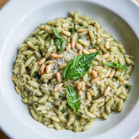 This photo displays a steaming bowl of 15-Minute Creamy Pesto Risoni, garnished with fresh basil.