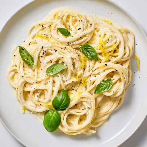 A steaming bowl of vegetarian Lemon Ricotta Pasta with spaghetti noodles coated in creamy ricotta and lemon sauce, topped with fresh herbs.