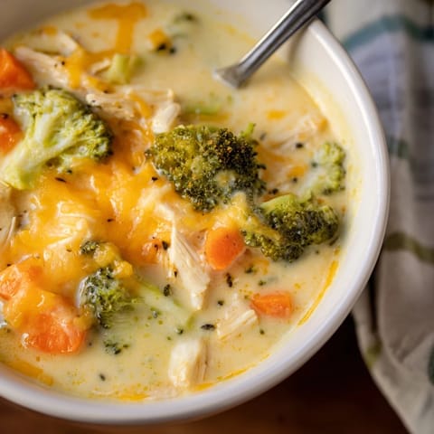 Steaming bowl of homemade Chicken Broccoli Cheddar Soup, with chunks of chicken, fresh broccoli, and carrots in a velvety cheddar broth.  