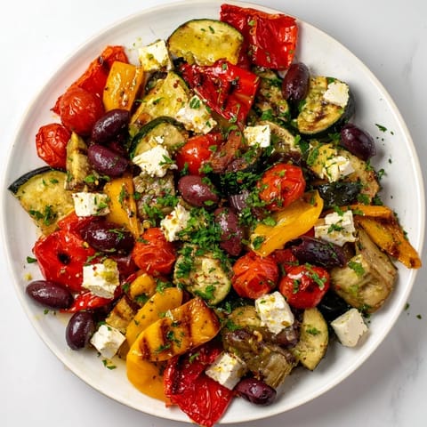 A close-up of Roasted Greek Salad shows juicy tomatoes and red onion wedges glistening with a zesty lemon-oregano vinaigrette.