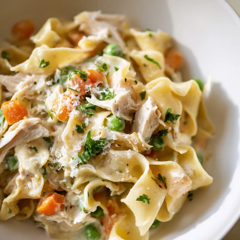 A close-up of the Spring Chicken Noodle Skillet highlights sweet peas, diced carrots, and savory chicken melding into a comforting, creamy pasta dish perfect for spring.
