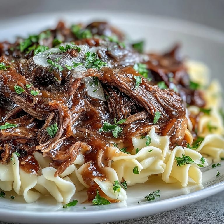 A comforting bowl of Crockpot French Onion Pot Roast Pasta with juicy beef, melted Gruyère, and fresh parsley garnish on a rustic table.