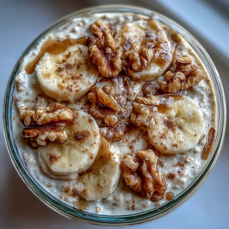 Creamy banana bread overnight oats with crunchy walnuts and fresh banana slices, served chilled in a rustic mason jar for a healthy morning treat.  