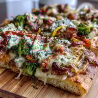 Vibrant St. Patrick's Day rainbow veggie flatbread pizza with colorful bell peppers, broccoli, and cherry tomatoes arranged in a festive pattern.
